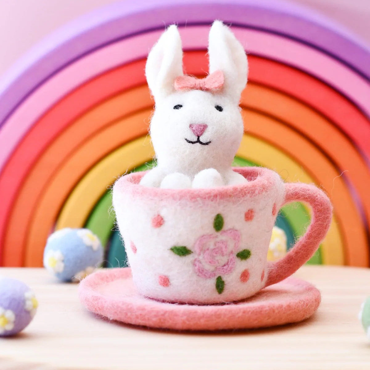 Felt toy rabbit in a pink teacup with a rainbow background