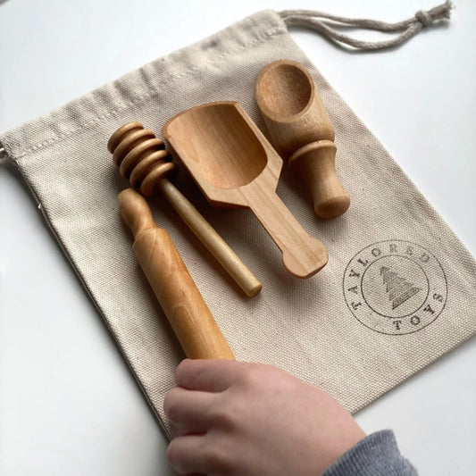 Set of wooden toy kitchen utensils including a honey dipper, scoops, and rolling pin with a beige drawstring bag.