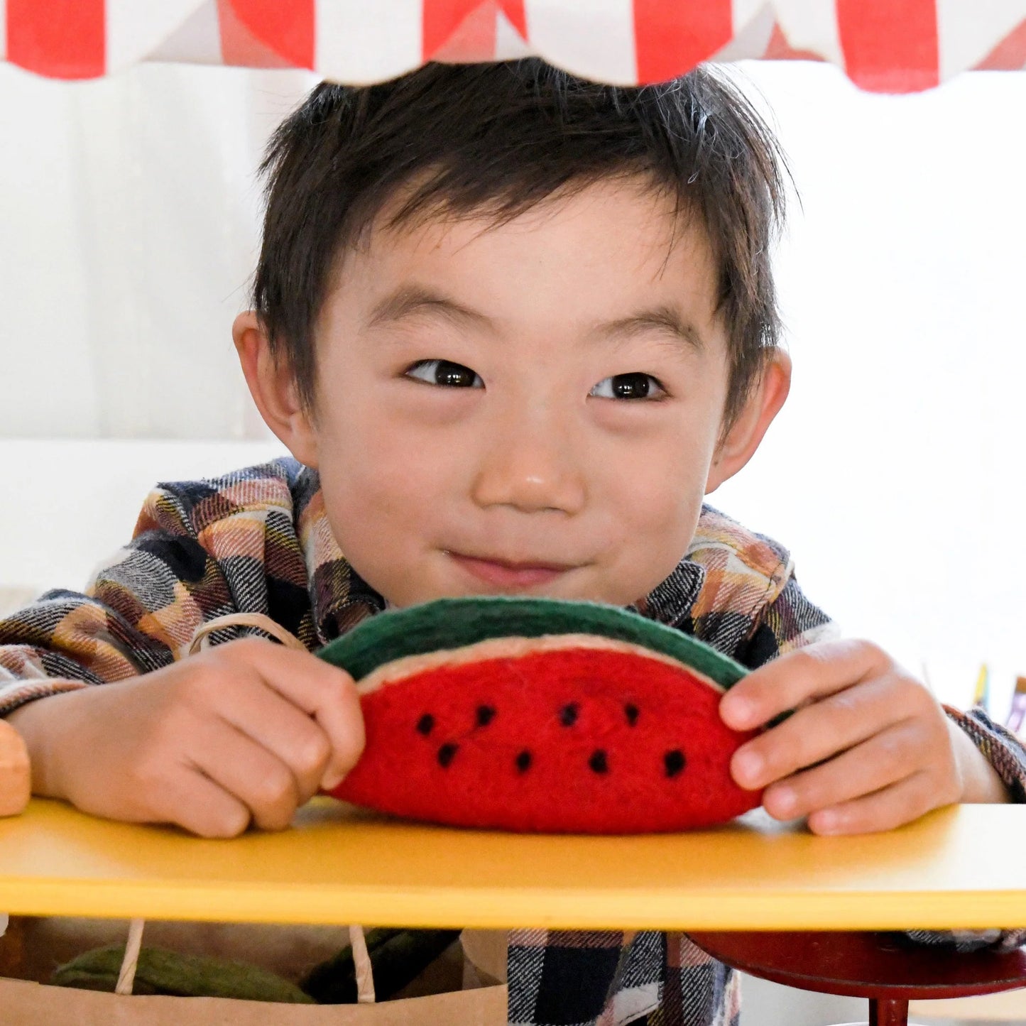 Boy in a pretend market stall holding a felt watermelon play food toy