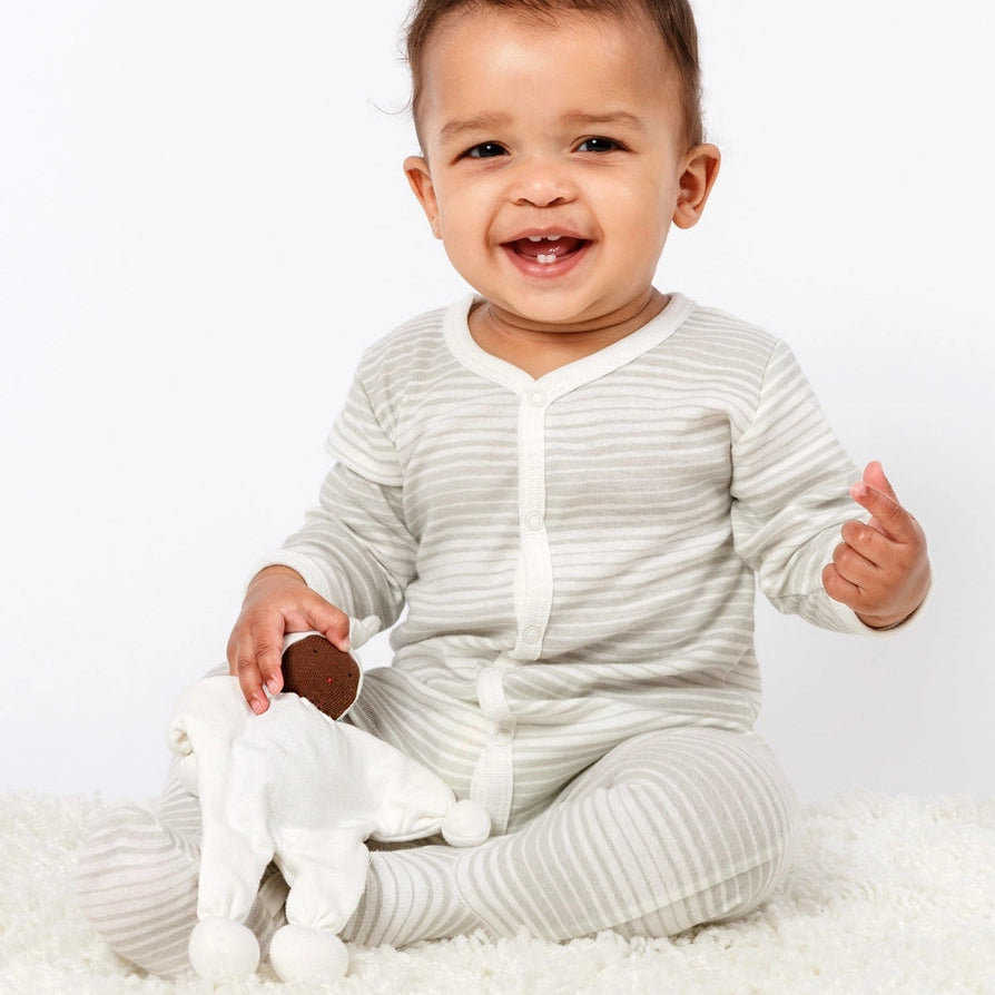 Baby holding Under the Nile Organic Baby Buddy Lovey with brown skin wearing solid white