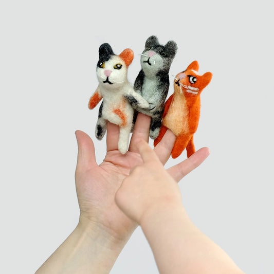 Felted cat finger puppets on a hand. One calico, one gray and one orange