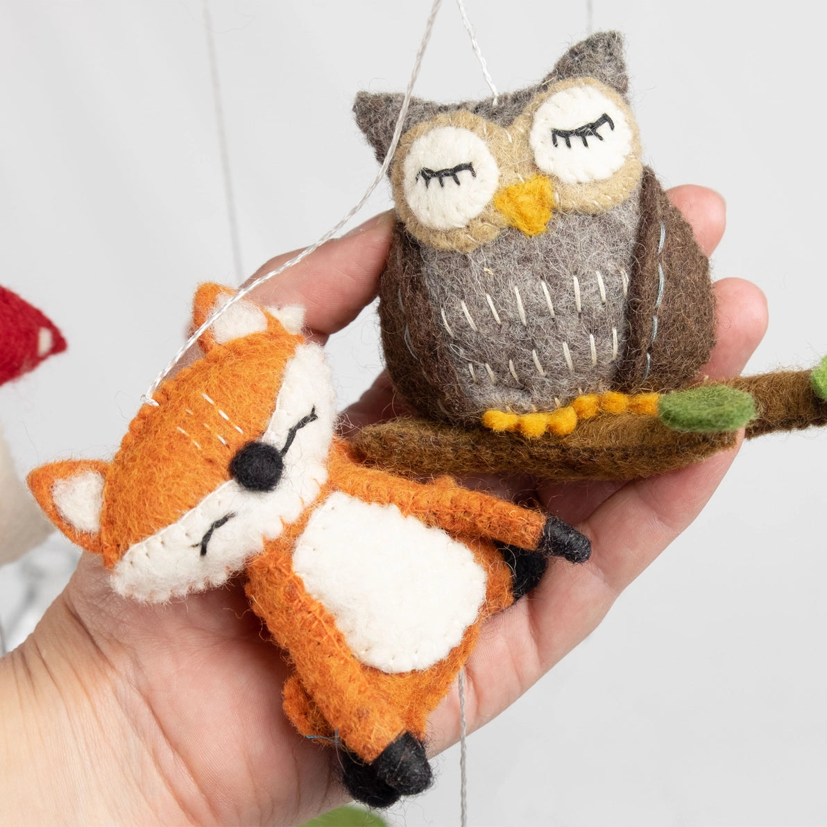 Hand holding two felt animal ornaments, an owl and a fox