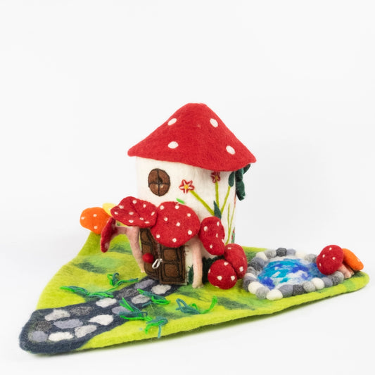 Felt Mushroom fairy house with a red dotted roof on a playscape with a stone path and a pond. 