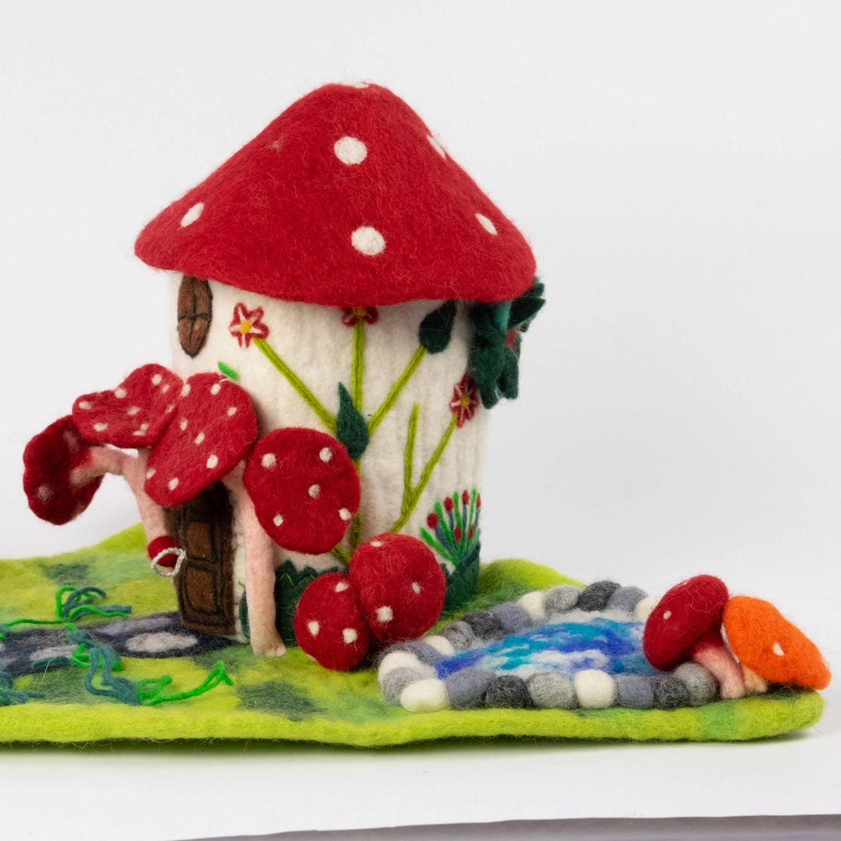 Felted Mushroom fairy house with flower embellishments and a nearby pond.