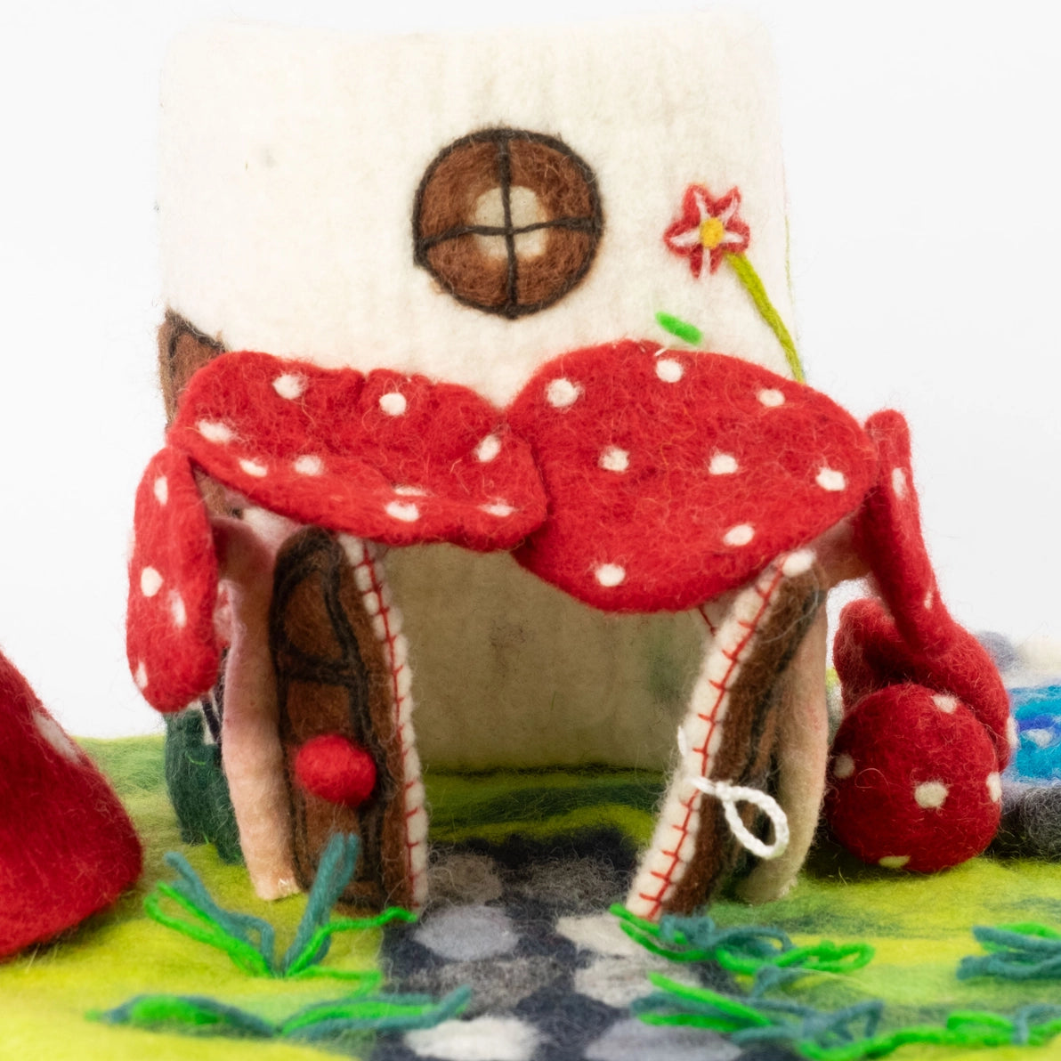 Felted mushroom fairy house with double doors that open onto a playscape with a stone path.