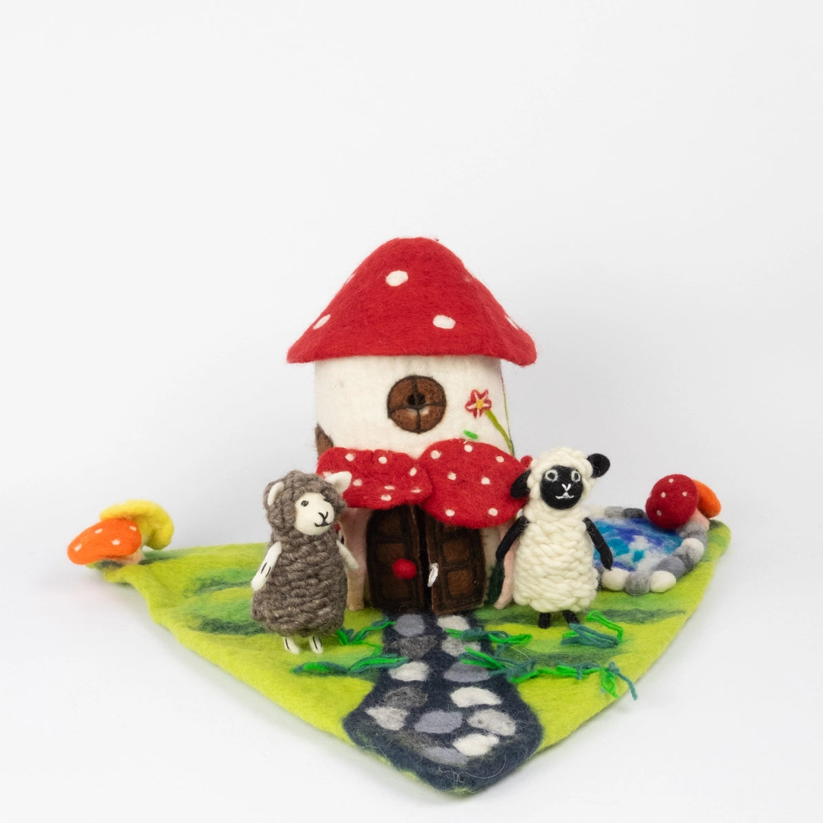 Felted Toy mushroom house with miniature sheep dolls on a forest playmat with a stone path and a pond.