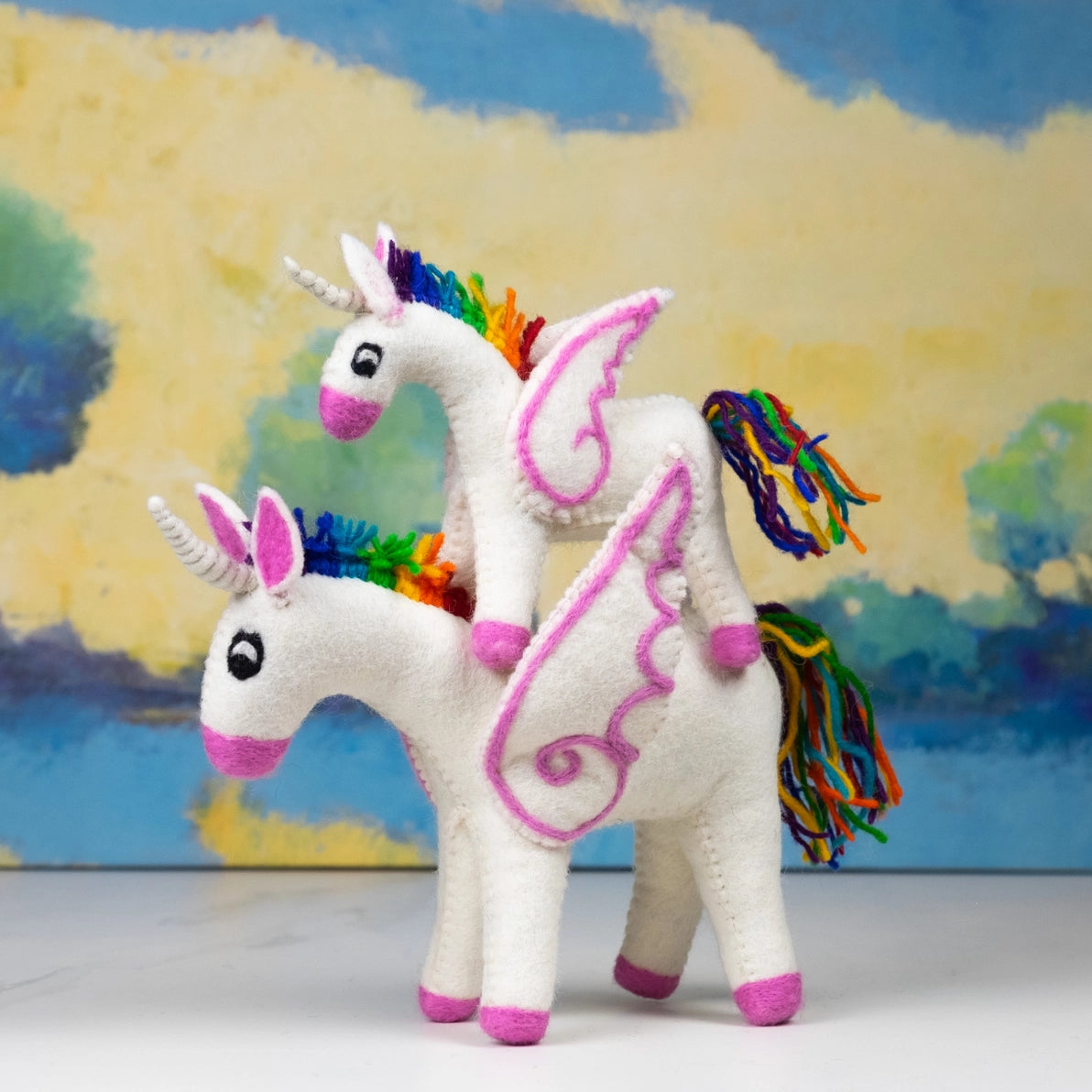 Two colorful felt unicorn toys with rainbow manes .