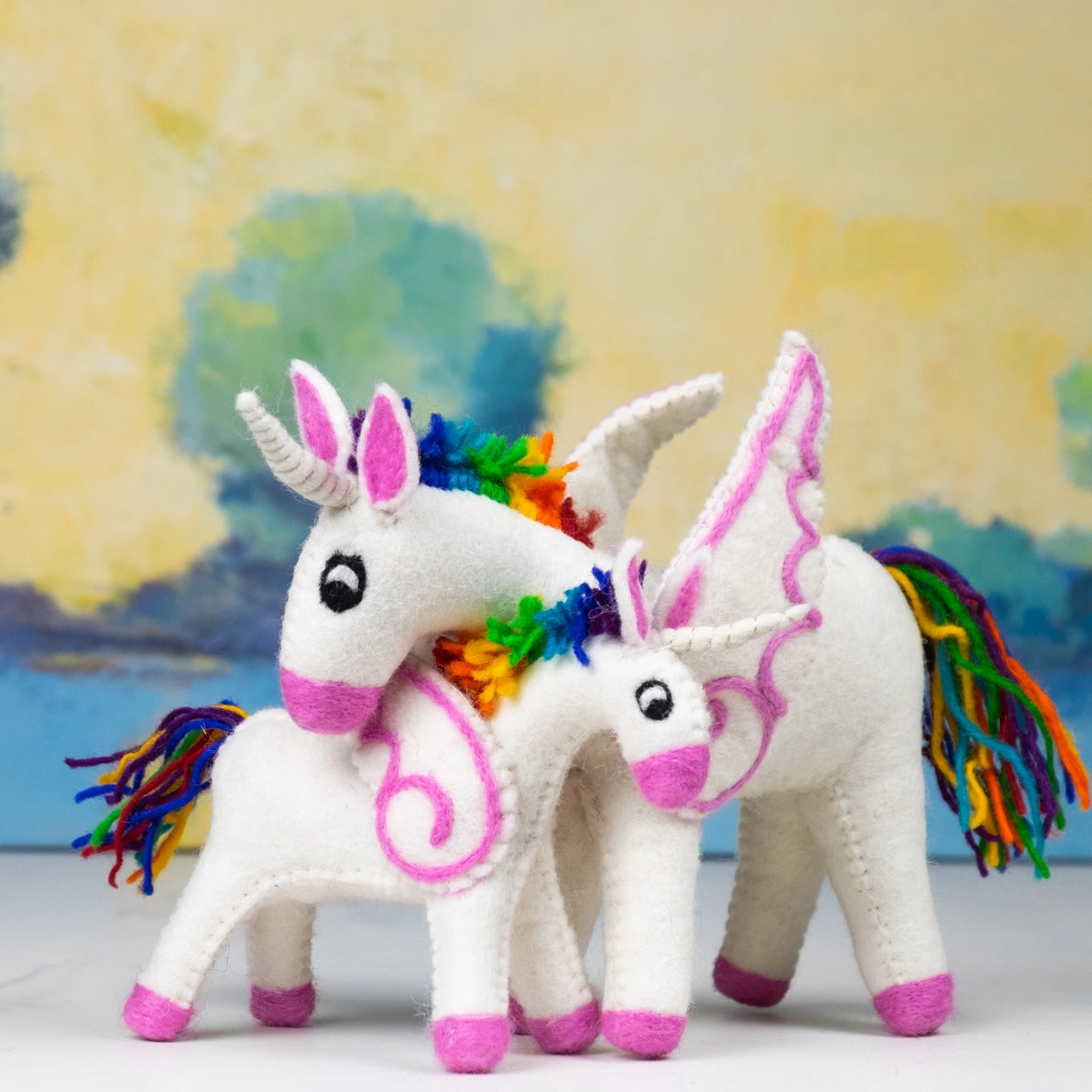 Two colorful felted unicorn toys with rainbow manes and tails.