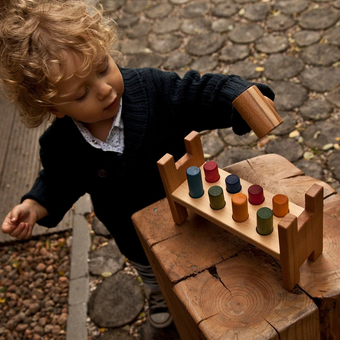 child playing with  Wooden Story Pound-a-peg toy with rainbow-colored pegs and hammer. 