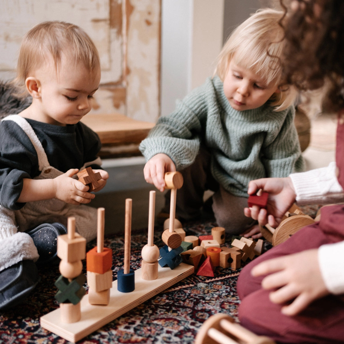 Three children playing with Wooden Story stacking and sorting shapes toy.